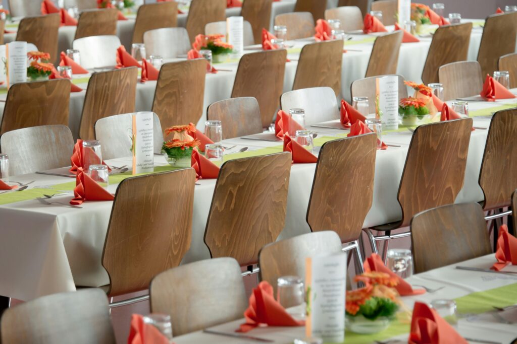 Beautifully arranged tables with wooden chairs for a formal event, adorned with orange flowers.